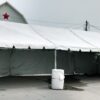 Side of the 20' x 50' Frame tent with partial side walls and water barrels used for ballast/tent anchoring.