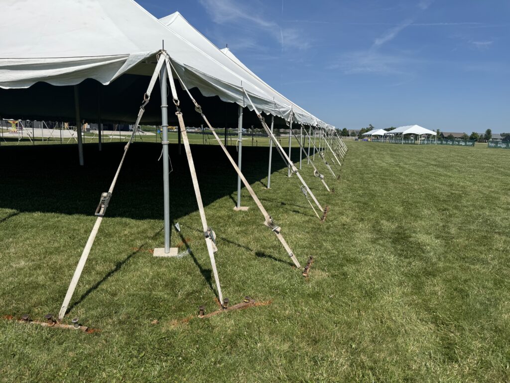 The corner of the 80′ x 120′ Rope and Pole Tent with gang tent stake bar (plate) with tent stakes and two 20′ x 60′ frame tents (right) at North Liberty Blues & BBQ at Centennial Park in 2026