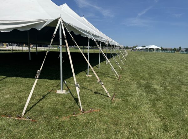 The corner of the 80′ x 120′ Rope and Pole Tent with gang tent stake bar (plate) with tent stakes and two 20′ x 60′ frame tents (right) at North Liberty Blues & BBQ at Centennial Park in 2026 The corner of the 80′ x 120′ Rope and Pole Tent with gang tent stake bar (plate) with tent stakes and two 20′ x 60′ frame tents (right) at North Liberty Blues & BBQ at Centennial Park in 2026