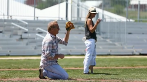 Kevin Costner plays catch with his son at the 25th anniversary of the movie Field of Dreams in Dyersville, Iowa with Bleachers by Big Ten Rentals in the background.