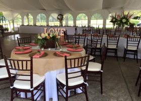 Tables and chairs setup under wedding tent with drape and chandeliers