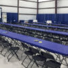 Tables and chairs setup for indoor event with booths in the background