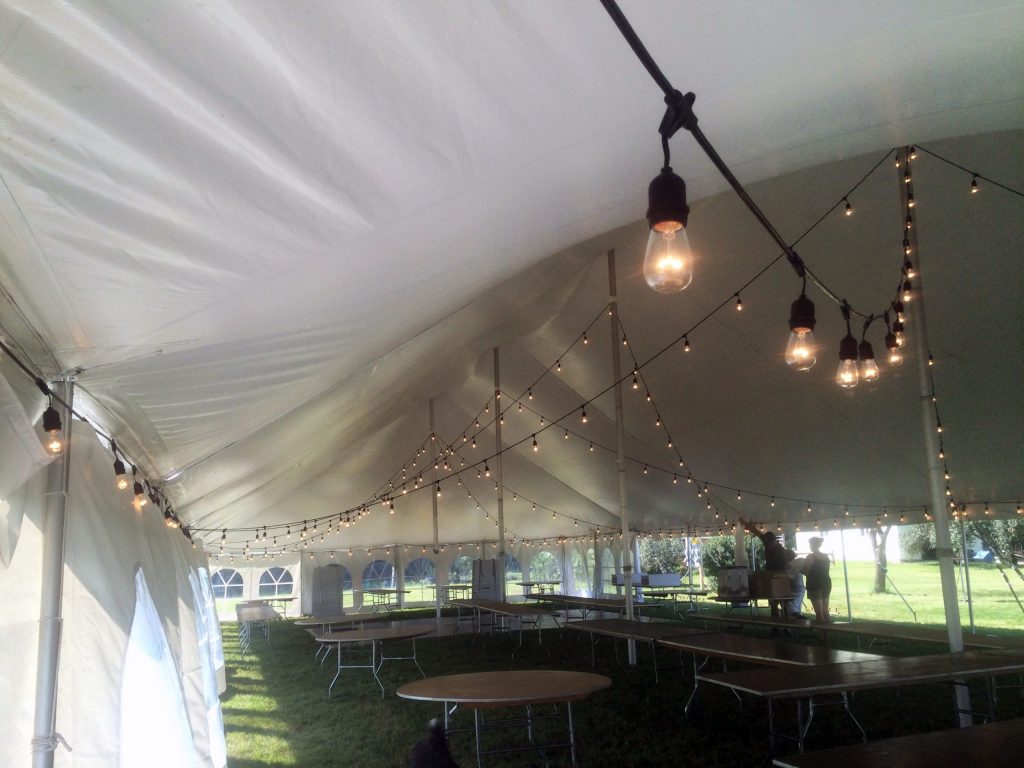Under of 40' x 100' rope and pole wedding tent with Edison lighting and French window sidewalls