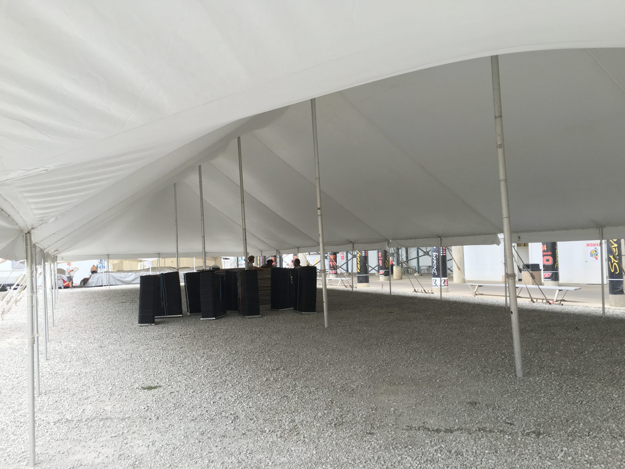 Under a 40' x 120' rope and pole tent at Knoxville Raceway (Marion County Fairgrounds) in Iowa with black chairs