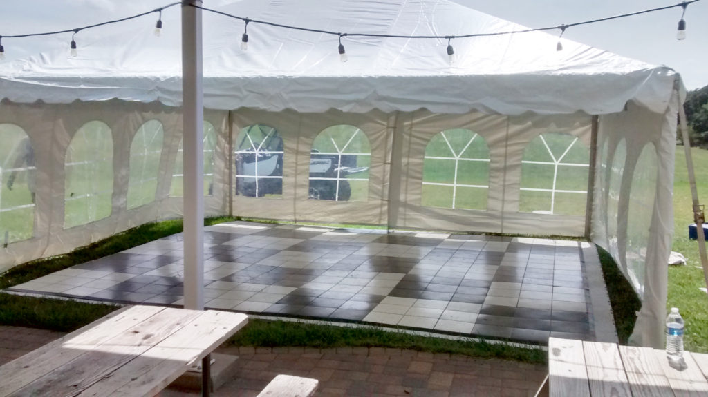 Black and white checked dance flooring under a 20' x 20' frame tent for 50s style anniversary party