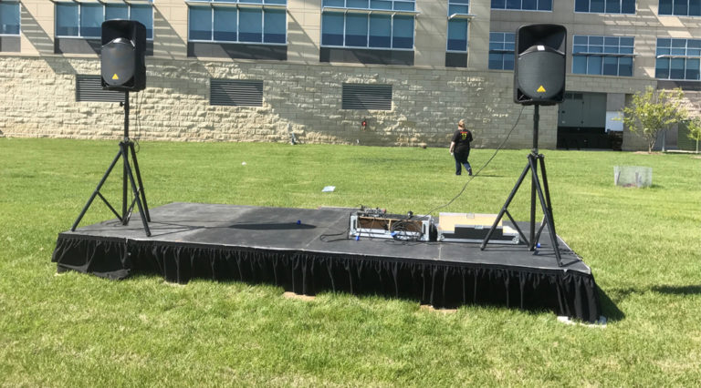 8′ x 16′ stage with PA sound package & tripods behind UICCU Financial Center Building in North Liberty, Iowa