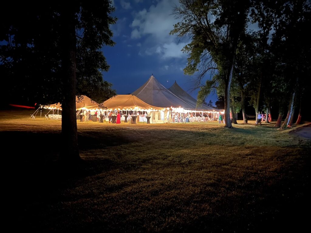 Two 20' x 30' canopy tents, and a large 60' x 90' legend twin-pole rope and pole tent at night.