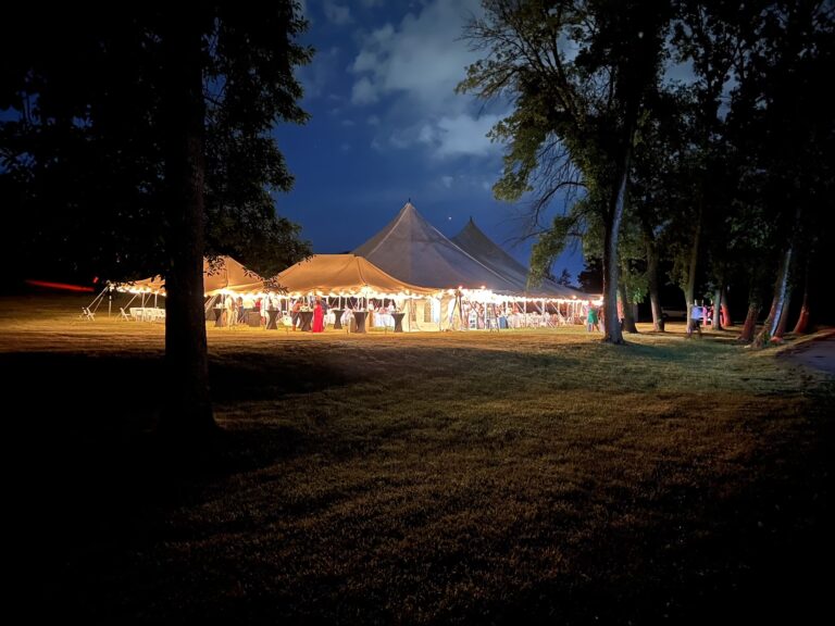 Two 20' x 30' canopy tents, and a large 60' x 90' legend twin-pole rope and pole tent at night.