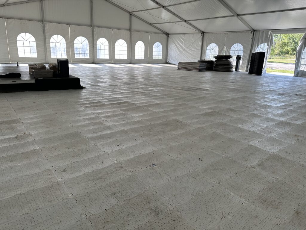Under the 60′ x 66′ (18m x 20m) Losberger clearspan structure temporary tent with temporary subflooring, stage, tables and chairs