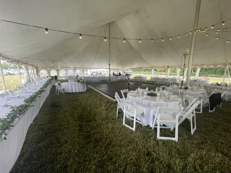 Wedding head table along with round tables and chairs, dance flooring and lights under a 60' x 90' legend twin-pole rope and pole tent.