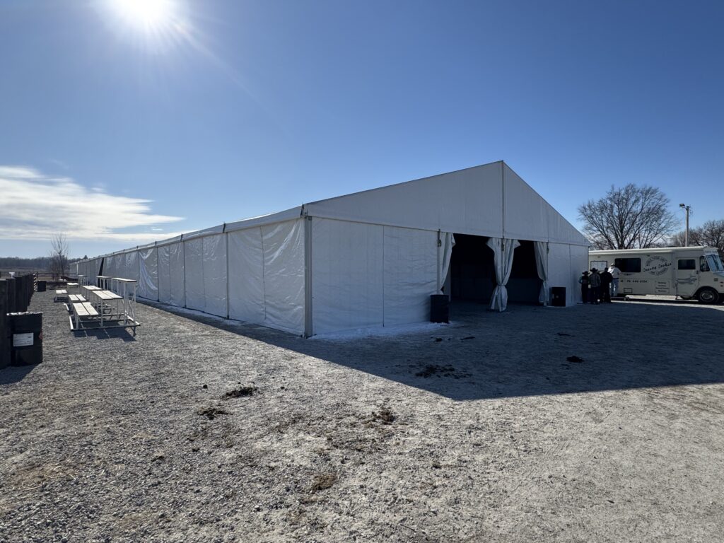 Outside of the 60' × 230' Losberger Clearspan tent at the Kalona Sales Barn at the 2026 Special Workhorse Sale with people (wide)
