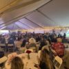 A crowd of people seated at round tables under a 40′ x 120′ Jumbo Track event tent in Iowa.
