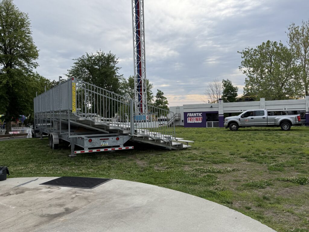 Side/rear view highlighting the towable trailer, Frantic Freeway ride building, and tall tower with red/white/blue accents at Adventureland Park in Altoona, Iowa.