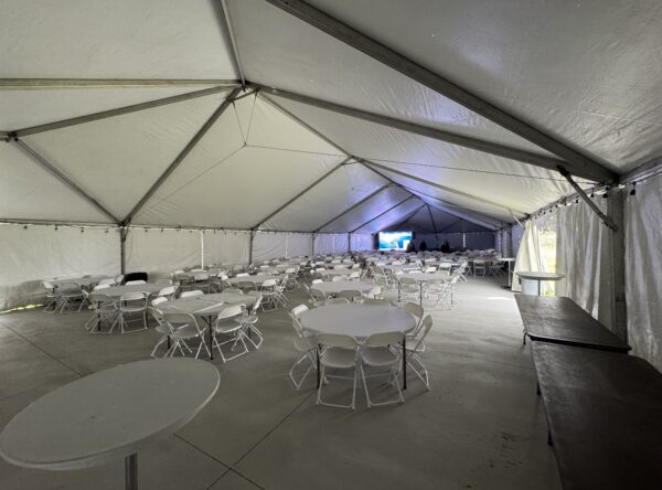 Under the 40′ x 120′ Hybrid Jumbotrac Event Tent with tables and chairs in the corner. Under the 40′ x 120′ Hybrid Jumbotrac Event Tent with tables and chairs in the corner.
