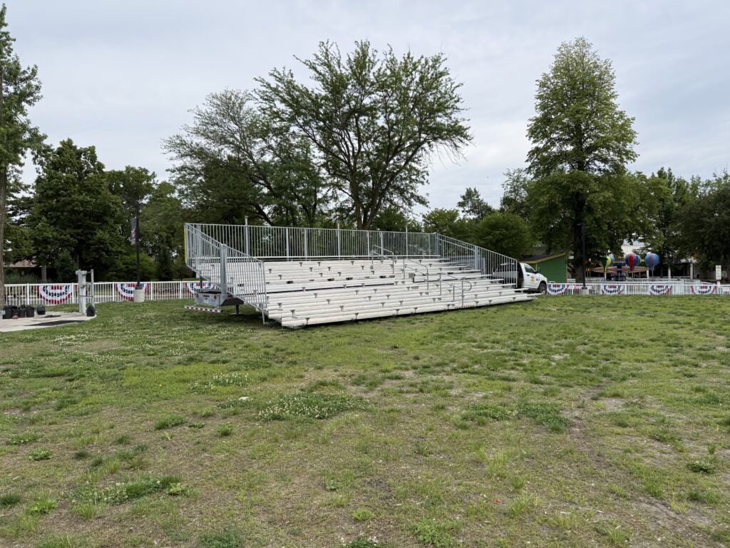 Wide shot showing full bleacher, fence with bunting, trees, and grassy field at Adventureland Park in Altoona, Iowa.