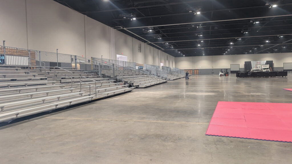 Close-up side angle of installed 45-foot bleachers with safety rails next to pink competition mats.